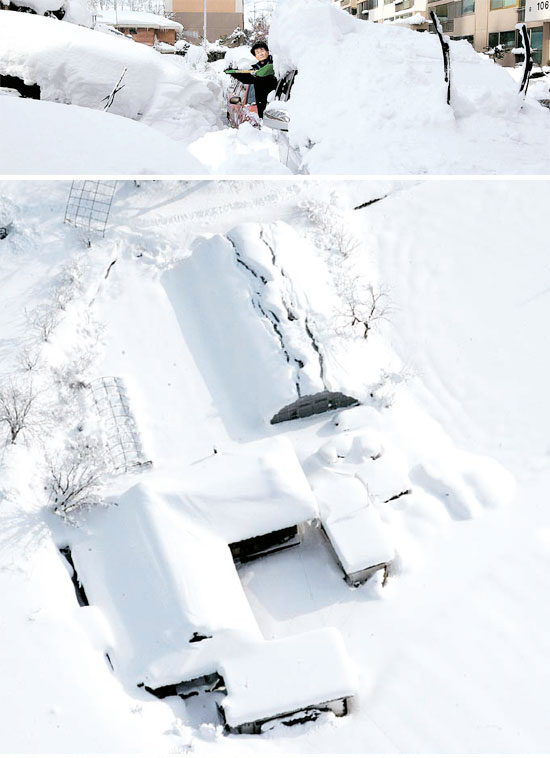 １３日、車の周辺の雪を片付けている東海市川谷洞のマンション住民（上）、雪の中で孤立している江陵市郊外の農村（下）。