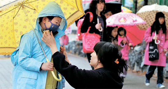 ７日、大田市関雎洞の仙岩（ソンアム）小学校の前で７日朝、父兄が登校する子どもの雨具を着せ直している。