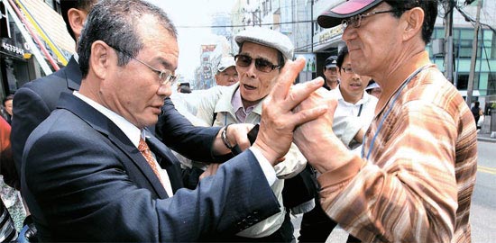 １３日、釜山（プサン）貯蓄銀行本店を訪問した李昇雨（イ・スンウ）預金保険公社社長（左）が座り込み中の預金被害者から激しい抗議を受けている。