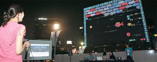 市民がソウル駅の前で、ソウルスクエアの建物をモニターにしてブロック崩しなど草創期のビデオゲームをしている。