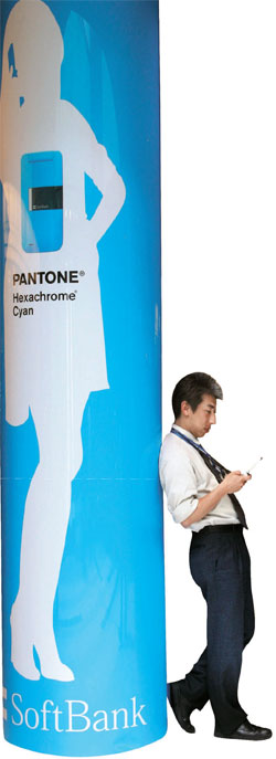 ２００７年５月、ある日本人男性がソフトバンク通信サービスの広告イメージが巻かれた柱にもたれて携帯電話の画面を見ている。（写真提供＝ブルームバーグ）