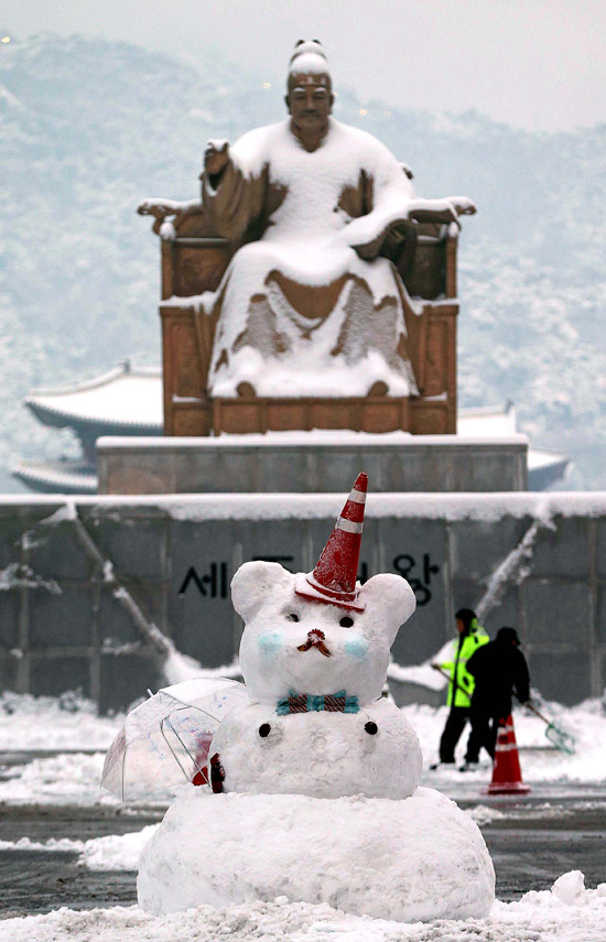 ４日、ソウル光化門（カンファムン）広場の世宗（セジョン）大王像と市民が作った雪だるまの間で市庁の職員が雪かきをしている。