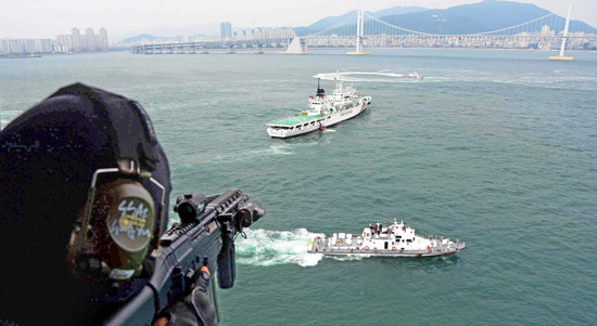 ヘリコプターに乗った海上警察特攻隊員が照準射撃の姿勢でテロ犯が占領した船舶を注視している。