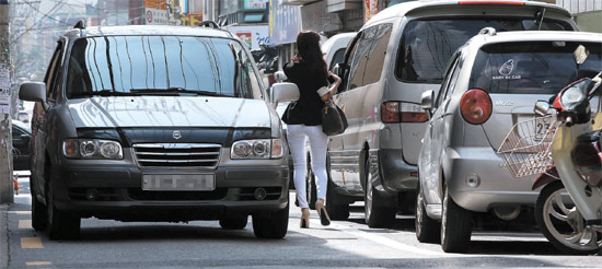 １５日、ソウル江西区禾谷１洞の道路で女性が向かってくる車と駐車した車の間を歩いている。この道路は歩道と車道が区分されていない幅９メートル未満の生活道路だ。