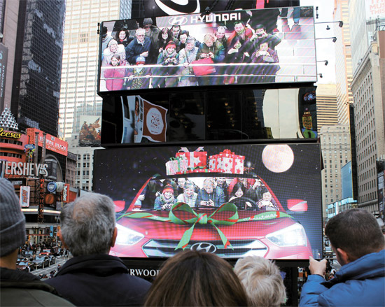 米ニューヨーク・タイムズスクエアの現代車広告看板の前で、市民が車に乗っているように合成された写真を見ながら笑っている。（写真＝現代車）