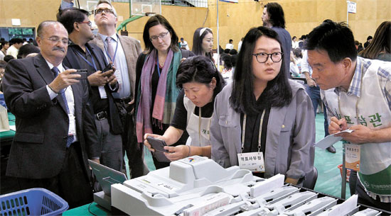４日午後、ソウル清雲洞（チョンウンドン）京畿商業高校体育館に設けられた開票所で開票状況を見守っている国際選挙参加団の団員（左）。