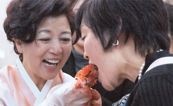 昨年１２月７日、東京の韓国大使館で開かれたキムジャン（キムチ作り）お祭りで、李丙ギ大使の夫人シム・ジェリョン氏（左）が安倍首相の夫人昭恵氏にキムチを食べさせている。この日、李大使は和食とキムジャン文化がユネスコ人類無形遺産に登録されたことに言及し、両国が互いに配慮するべきだと強調した。（写真＝中央フォト）