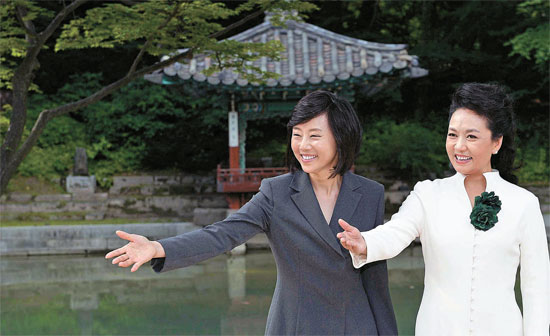 白いスカートとロングジャケットに濃いグリーンの花形ブローチをつけた彭麗媛夫人（右側）が３日、趙允旋（チョ・ユンソン）政務首席と共に昌徳宮（チャンドックン）境内を見学している。