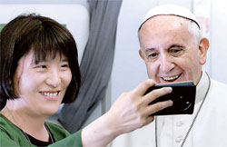 １４日、法王チャーター機で中央日報のコ・ジョンエ特派員がフランシスコ法王と一緒に写真撮影をしている。（写真＝米カトリック専門通信社ＣＮＳポール・ヘリン記者）