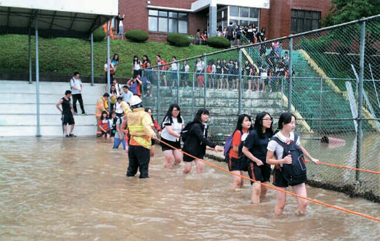 ２５日午後、釜山・陽徳女子中学校の生徒たちが消防隊員の案内を受けて緊急避難している。同校は１階の教室１０カ所余りが水と土砂の被害に遭った。（写真提供＝釜山消防本部）