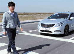 １４日、華城交通安全公団自動車安全研究院の走行試験場で研究員が横断歩道を渡っている。その前に近づいた自律走行車はレーダーで人を感知し自動で止まる。（写真＝現代モービス）