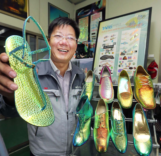 ウィグコリア（ＷＩＧＫＯＲＥＡ）のソ・ソンイン代表が、見る角度によって多彩に色が変わる特殊素材ルビオレ（Ｌｕｖｖｉｏｌｅ）で作った靴のサンプルを持ち上げて笑っている。