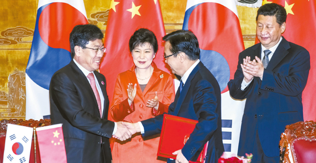 尹相直産業通商資源部長官（左）と高虎城中国商務相（左から３人目）が１０日、中国北京人民大会堂で韓中自由貿易協定（ＦＴＡ）交渉終了に関する韓国政府と中国政府の合意議事録に署名した後、握手している。これを見る朴大統領（左から２人目）と習近平国家主席（右）が拍手している。（写真＝青瓦台写真記者団）