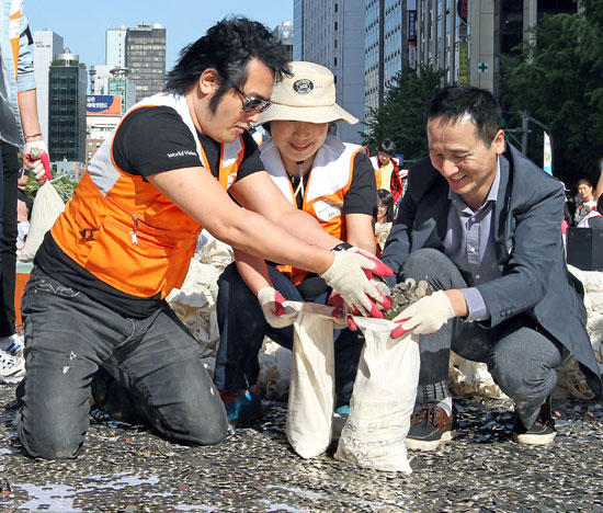 ５日、ソウル清渓広場で俳優キム・ボソン（写真左）とボランティアメンバーがコインを回収している。