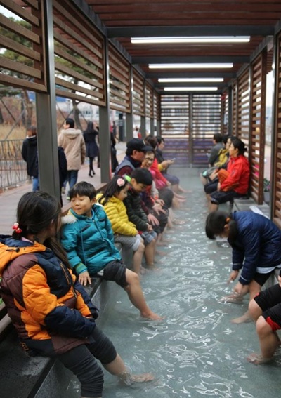 仁川松島にある露天足湯場で市民や子供たちが足湯体験を楽しんでいる。（写真＝仁川経済自由区域庁）