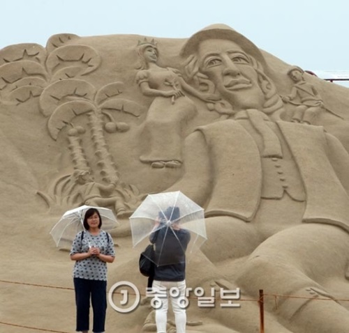 ６日、釜山の海雲台海水浴場で開催されている砂祭りに出品された砂像作品を楽しんでいる観光客ら。