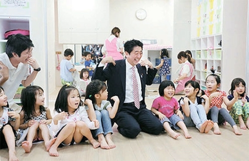 安倍晋三首相（中央）が２０１３年に横浜市の保育所で授業を参観している。安倍首相は少子化克服に向け内閣府にコントロールタワーを作った。（写真＝内閣府ホームページ）