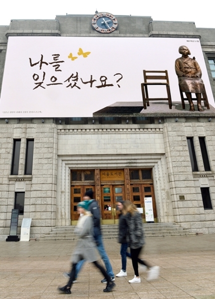 昨年２月、平和の少女像・写真と共に慰安婦被害者キル・ウォンオクさん（８９）の手書き文字が印刷された大型垂れ幕がかかったソウル市庁前のソウル図書館。
