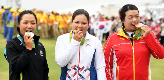 リオ五輪女子ゴルフで優勝した朴仁妃（中央）、銀メダルのリディア・コー（ニュージーランド、左）、銅メダルの馮珊珊（中国）がメダルをかむポーズを取っている。（写真＝五輪写真共同取材団）