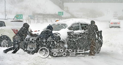 １４日、江原道の大関嶺マウルのサービスエリアの駐車場で、雪で立ち往生してしまった乗用車をドライバーが道路側に押している。