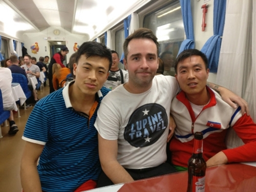 １２日、平壌へ向かう列車で北朝鮮アイスホッケーチームの選手と写真を撮るルパイン旅行会社のガイド、ジェームズ・ピナティさん。（写真＝ルパイン・トラベルのフェイスブック）