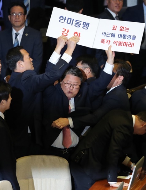 大韓愛国党の趙源震議員がトランプ米大統領の演説を控えた８日午前、国会本会議場で「韓米同盟強化」「朴槿恵前大統領釈放」と書かれたカードを掲げ、国会事務局の関係者から制止されている。