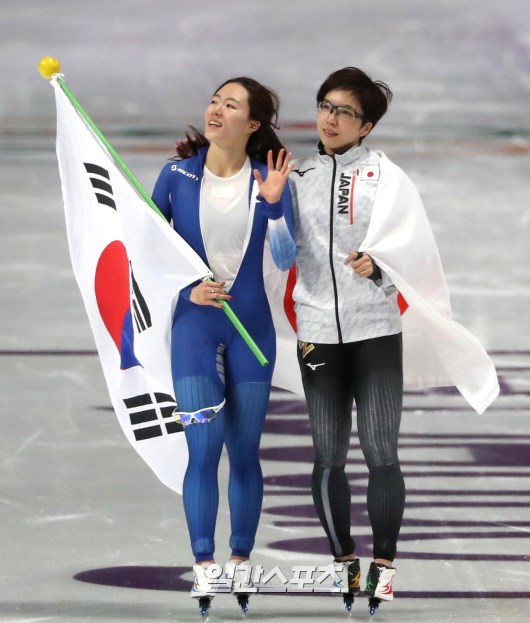 ２０１８年平昌冬季五輪スピードスケートの競技が１８日午後、江陵スピードスケート競技場で開かれた。スピードスケート女子５００ｍに出場した李相花が銀メダルを確定した後、太極旗を手に観衆の応援に応えている。その横は金メダルを獲得した日本の小平奈緒。