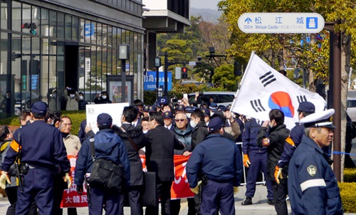 ２０１３年、島根県が主催した「竹島の日」行事場所の外で独島守護全国連帯など韓国の市民団体会員が日本の警察に囲まれながら太極旗を持って抗議デモを行っている。
