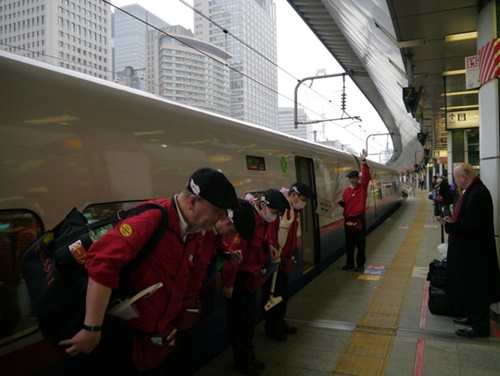 東京駅に新幹線の列車が到着し、清掃直前に赤いユニホームを着たテッセイ（ＴＥＳＳＥＩ）のスタッフが内方線（安全線）の外側に整列して利用客に挨拶している。かばんには各種清掃道具が入っている（写真＝中央フォト）