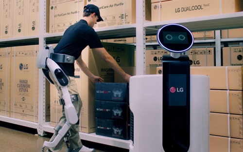「ＬＧ ＣＬＯｉ　ＳｕｉｔＢｏｔ」を着た作業者が物流センターで商品をショッピングカートロボットに入れている。（写真＝ＬＧエレクトロニクス）