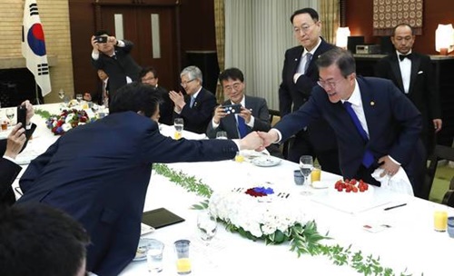 文在寅大統領（右）が昨年５月９日、東京の首相官邸で開かれた韓日首脳会談の昼食会で、安倍首相から大統領就任１周年記念ケーキを受けた後、首相と握手している。（青瓦台写真記者団）