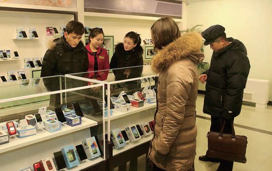 平壌のある携帯電話売り場に陳列されたスマートフォンを見る市民。利用に制約がある独自生産製品のほか中国から持ってきた中古機器も密かに取引される。［写真　北朝鮮対外宣伝メディアウェブサイト］