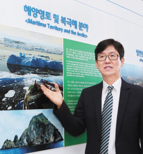 キム・ジョンドク韓国海洋水産開発院（ＫＭＩ）政策動向研究本部長が釜山にある研究院１階広報館で北極海を航行する砕氷船の写真を背景に北極航路の重要性を説明している。ソン・ボングン記者