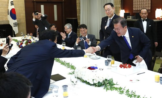 韓国の文在寅大統領が２０１８年５月９日、東京の首相公館で開かれた韓日首脳会談昼食会で、安倍晋三首相から大統領就任１周年記念を祝うケーキを受け取った後、首相と握手している。［写真　青瓦台写真記者団］