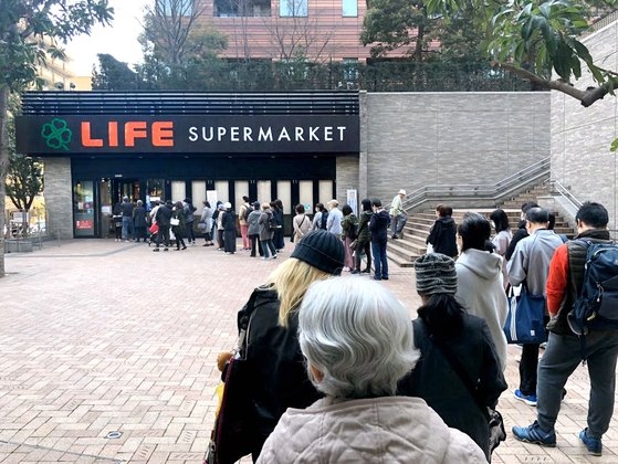 ２５日、東京のある大型スーパーの前に、食料品を買い求める人々列をつくっている。