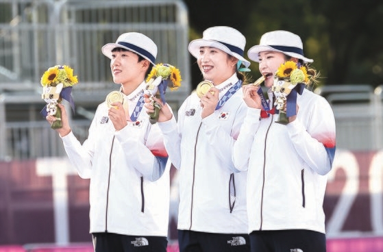 韓国が２５日、五輪アーチェリー女子団体戦で９回連続で金メダルを獲得した。アーチェリーに団体戦が導入された１９８８年のソウル大会から１度も金メダルを逃していない。表彰台に上がった左からアン・サン、チャン・ミンヒ、カン・チェヨン選手が金メダルと花束を持ち上げて見せている。［写真　五輪写真共同取材団］