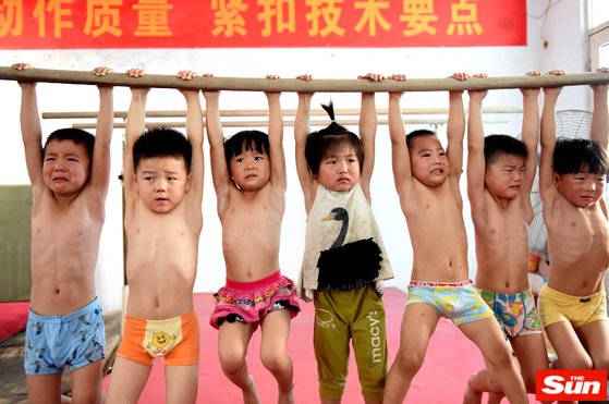 中国のスポーツ英才訓練の様子。４歳くらいの子どもたちが涙を流しながら鉄棒をつかんでいる。［サン　キャプチャー］