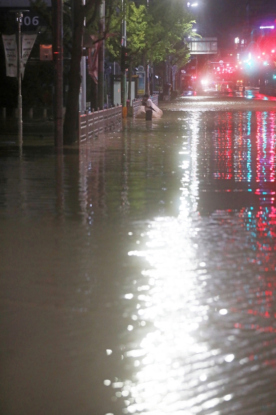 ２４日午前、釜山蓮堤区（プサン・ヨンジェグ）の瓜亭（クァジョン）交差点である市民が激しい雨で浸水した距離を渡っている。［写真　ニュース１］