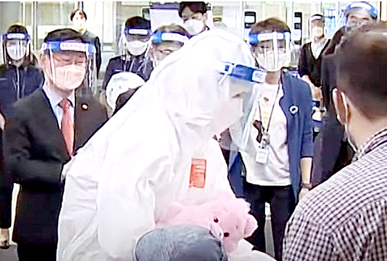 今月２６日、防疫服を着た韓国法務部関係者が仁川（インチョン）国際空港に入国したアフガニスタン特別入国者などに人形を手渡している。この日法務部は、入国場面を取材する記者団に朴範界（パク・ポムゲ）法務部長官（左）の「人形伝達式」を撮影してほしいと要求した。［写真　ＹｏｕＴｕｂｅキャプチャー］
