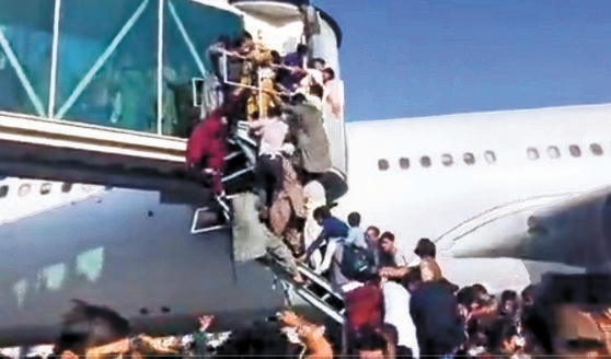 イスラム武装組織タリバンが政権を再掌握した今年８月１６日、首都カブール空港からアフガニスタンを脱出しようとする人々が航空機に乗ろうと搭乗ブリッジにぶらさがり混乱を来している。［写真　ツイッター　キャプチャー］