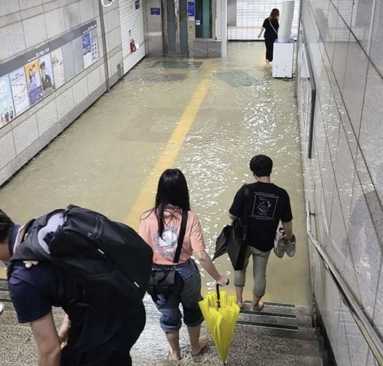 ３０日午前、豪雨特別警報が発令された中で、水原市勧善区（スウォンシ・クォンソング）地下鉄１号線の細柳（セリュ）駅地下通路が浸水し、出勤途中の市民が靴を脱いでプラットフォームに向かっている。［写真　ツイッター　キャプチャー］