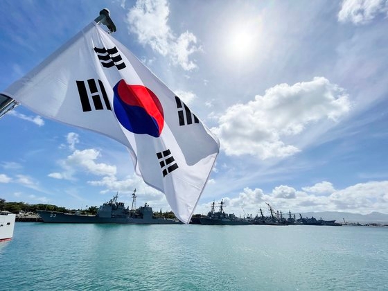 韓国駆逐艦「世宗大王」の艦尾に掲げられた太極旗の後方に各国から派遣された艦艇が真珠湾に停泊している。