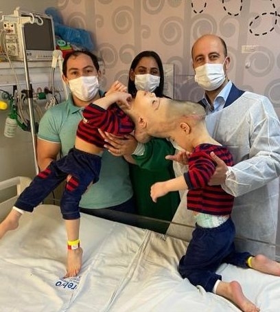 ブラジルで生まれた頭がつながった結合双生児の兄弟の姿。写真右側がＶＲ手術でリハーサル方式を試みた英国ロンドン・グレート・オーモンド・ストリート病院の神経外科医ヌール・ウル・オワセ・ジーラニ氏。［写真　英国の医療慈善団体ジェミニ・アントゥワインドのホームページ］