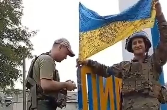 １日、ウクライナ軍が５月にロシア軍に占領された東部都市リマンに進入し、都市名が入った表示板に国旗を立てている。［写真　ウクライナ大統領秘書室長ツイッター　キャプチャー］