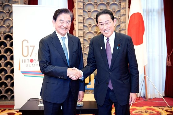 日本の岸田文雄首相（右）と洪錫炫中央ホールディングス会長が１１日午後、東京の首相公邸１階ホールで特別対談を終え握手している。幾何学模様の窓枠で装飾されたホールの壁には広島Ｇ７サミットのポスターが掲げられ、岸田首相もえりに同じＧ７エンブレムのバッジを付けた。チョン・ミンギュ記者