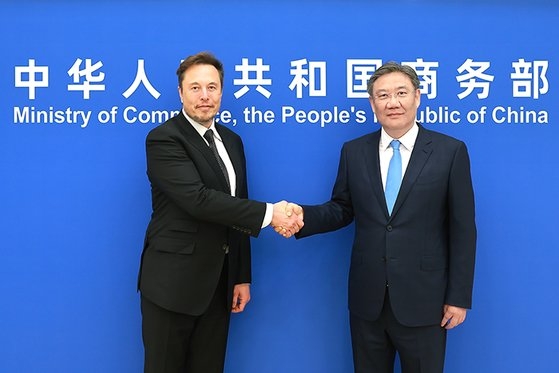 先月３１日、中国の王文濤・商務部長（右）が中国を訪問したテスラのイーロン・マスク最高経営責任者（ＣＥＯ）と会って握手をしている。［写真　中国商務部ホームページ］