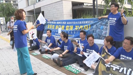 先月１０日、共に民主党など野党議員で構成された「福島核汚染水海洋投棄阻止国会議員団」が東京の参議院議員会館の前に座り、旗を振りながら歌を歌っている。　東京特派員映像記者団