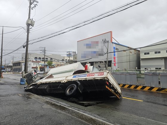 ２１日午前８時４５分ごろ、釜山市沙上区の道路で横１０メートル、縦５メートル、深さ８メートルの大型陥没が発生し車２台がはまる事故が起きた。最初は消防排水支援車両の一部がはまったが、近くを通りがかったトラックの重さに耐えられず道路がさらに崩れ２台とも完全にはまり込んだ。［写真　釜山消防災害本部］