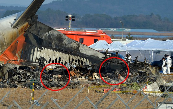 チェジュ航空機の乗客と乗務員１８１人中１７９人の死亡者が発生した務安国際空港の事故現場で１２月３０日午後、警察と消防隊員が合同で現場鑑識を実施している。事故原因と指摘された旅客機のランディングギア（赤い円内）はひどく破損している。キム・ソンテ