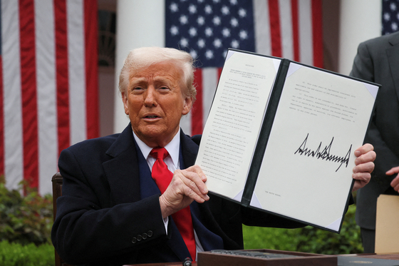   関税に関する大統領に署名し上げて見せるトランプ大統領。［写真　ロイター＝聯合ニュース］